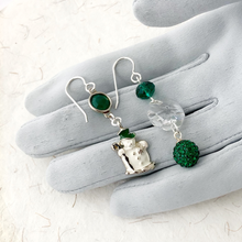 Load image into Gallery viewer, Asymmetric earrings in emerald and crystal with vintage snowman charm  displayed on a grey gloved hand
