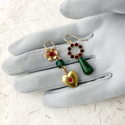 Festive asymmetric earrings on a grey gloved hand against a light background