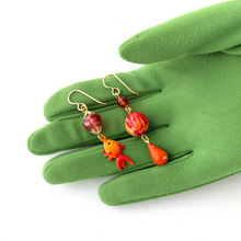 Load image into Gallery viewer, asymmetric earrings in red and orange with vintage koi charm displayed on a green gloved hand
