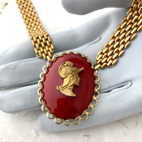 close-up of red and gold cameo necklace on a gloved hand
