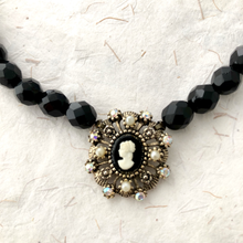 Load image into Gallery viewer, close-up of necklace with black beads and a decorative cameo pendant on a textured white background
