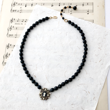 Load image into Gallery viewer, Black beaded necklace with a cameo pendant on a mixed paper background
