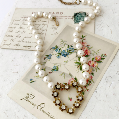 necklace with heart shaped focal set with flowers and rhinestones and vintage faux pearls on some vintage postcards