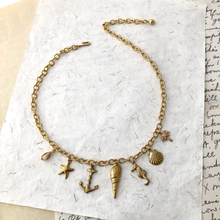 Load image into Gallery viewer, Gold toned charm necklace on a textured white surface
