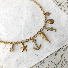 Load image into Gallery viewer, Gold toned charm necklace on a textured paper surface
