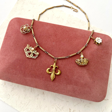 Load image into Gallery viewer, Gold toned necklace with unusual vintage charms on a pink velvet jewellery box
