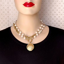 Load image into Gallery viewer, A gold-tone double-strand necklace with white faux pearls and a round gold pendant, wrapped twice  around the neck of a mannequin wearing a black top and red lipstick.
