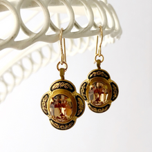 Load image into Gallery viewer, black and gold earrings with light topaz rhinestone centres  hanging from a white wire frame
