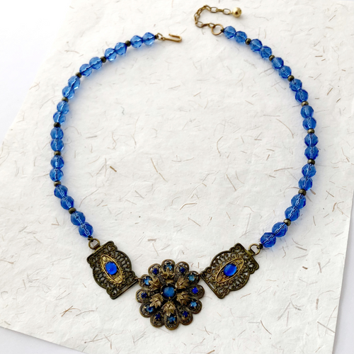 necklace with vintage brass filigrees, sapphire rhinestones, repurposed glass  beads and Pyrite beads on a flat background