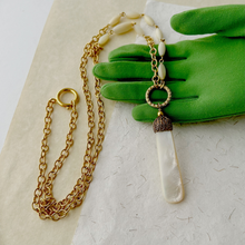 Load image into Gallery viewer, necklace with mother of pearl pendant and beads with gold chain displayed on a green gloved hand
