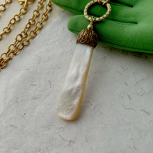 Load image into Gallery viewer, close up of necklace with mother of pearl pendant and beads with gold chain displayed on a green gloved hand
