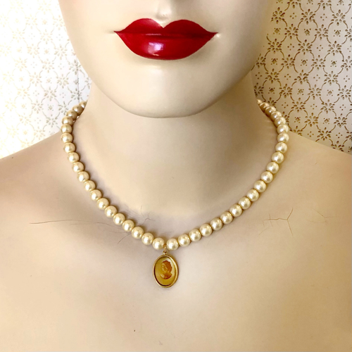Pearl necklace with vintage cameo  pendant on a mannequin with red lips against a decorative background