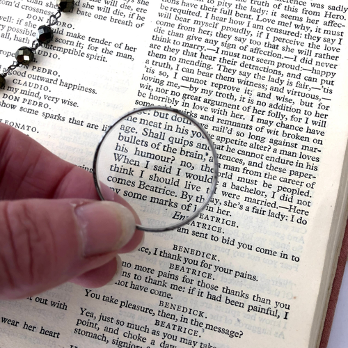 Hand holding a magnifying lens over an open book with text.
