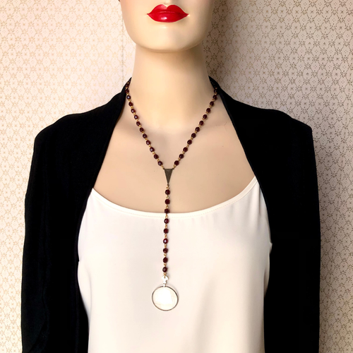 Mannequin wearing a black blazer and white top with a red beaded y-shaped necklace with a lens as a feature.