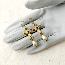 Load image into Gallery viewer, Gold cross earrings with pearl drops on a gray glove
