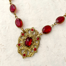 Load image into Gallery viewer, close up of medieval styled necklace with red gemstones and gold chain on a textured white background
