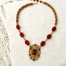 Load image into Gallery viewer, Medieval styled gold-tone necklace with red gemstones on a textured white surface with music sheet background
