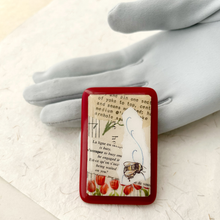 Load image into Gallery viewer, A rectangular red-bordered brooch featuring a vintage paper background with French text, tulip flowers, and a bee illustration, displayed on a white textured surface against a grey gloved hand
