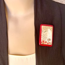 Load image into Gallery viewer, A rectangular red-bordered brooch featuring a vintage paper background with French text, tulip flowers, and a bee illustration pinned to the lapel of a dark brown-black jacket worn by a mannequin torso.
