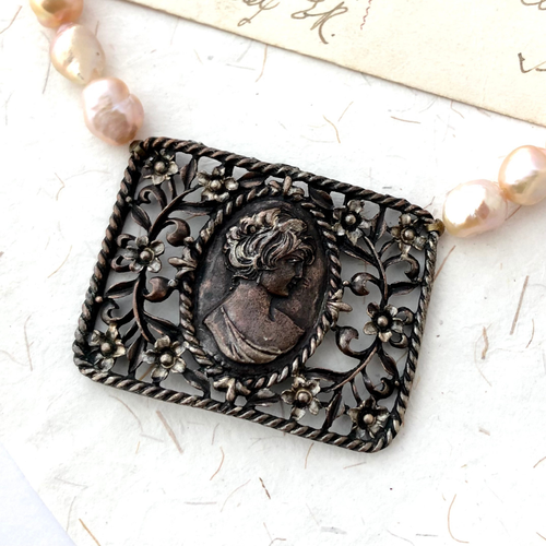 Close-up of vintage filigree cameo focal and freshwater pearls on paper background