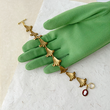 Load image into Gallery viewer, bracelet with flower shaped links and vintage cameo accent displayed on a green gloved hand

