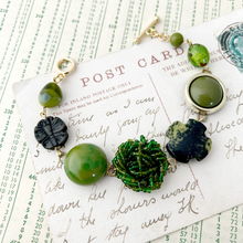 Load image into Gallery viewer, green toned bracelet made with vintage earrings and beads on a vintage postcard
