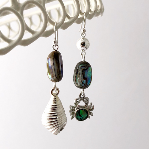 asymmetric earrings with Paua shell beads, crab charm and vintage Lucite shell charm hanging from a white frame