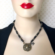 Load image into Gallery viewer, Necklace with a large shield-like pendant on a mannequin wearing a black top against a pale background
