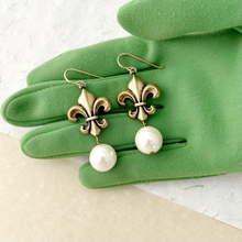 Load image into Gallery viewer, Antique bronze toned fleur-de-lis earrings with pearl drops on a green gloved hand
