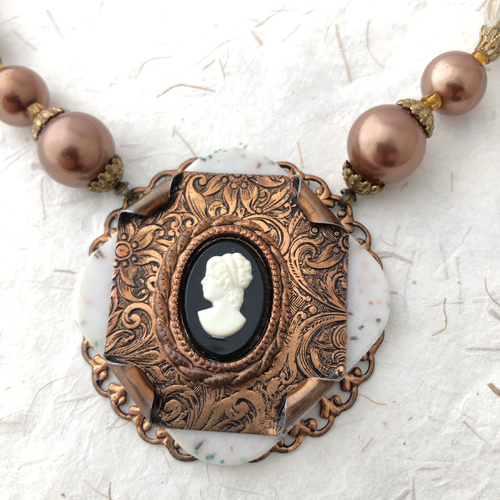 close-up of necklace with ornate cameo pendant and faux pearls on a textured white background