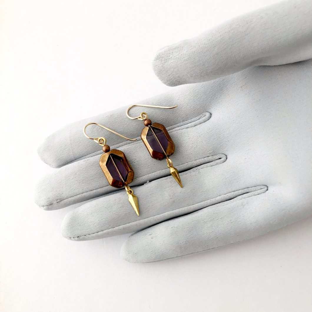 vintage amethyst glass stone earrings with gold edges and a brass dangle displayed on a gloved hand