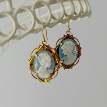 Load image into Gallery viewer, vintage blue resin cameo earrings in gold toned frames hanging from a white frame

