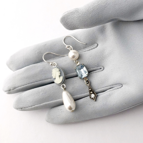 asymmetric earrings with blue cameo, rhinestones and pearl beads displayed on a gloed hand for size