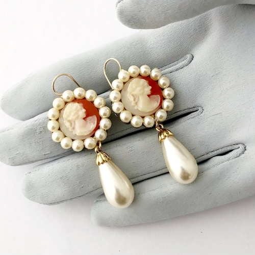 Pair of earrings with vintage cameos and pearls on a grey gloved hand