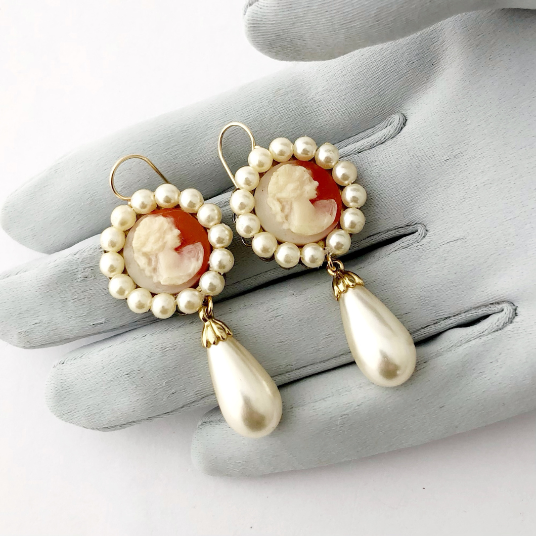 Pair of earrings with vintage cameos and pearls on a grey gloved hand