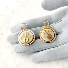 Load image into Gallery viewer, earrings in gold and cream featuring a banjo displayed on a grey loved hand

