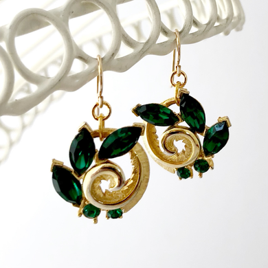 vintage gold toned swirled earrings set with green rhinestones hanging against a white background