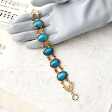 Load image into Gallery viewer, bracelet with large blue glass stones and gold links displayed on a grey gloved hand
