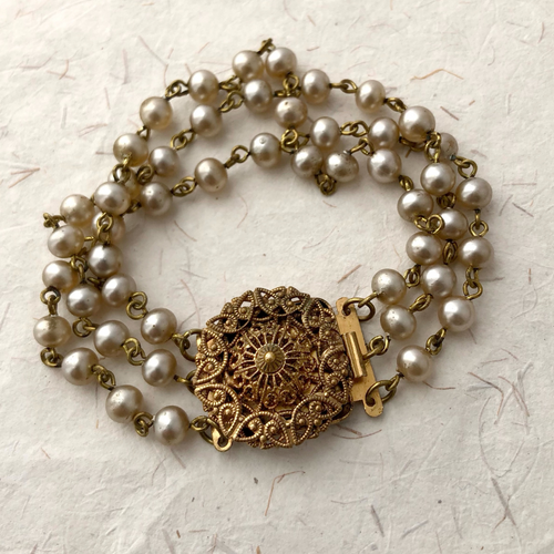 Pearl bracelet with a gold-toned filigree clasp on a textured beige background