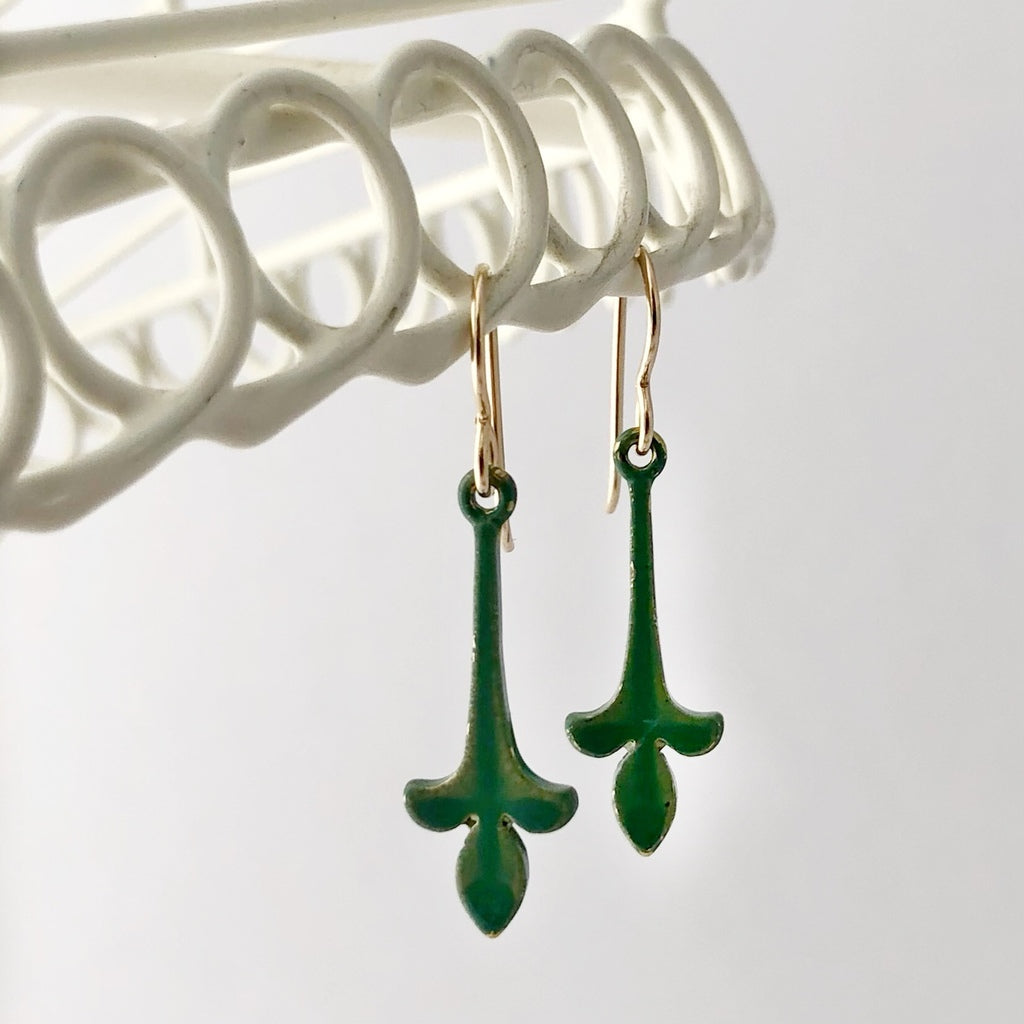 green fleur-de-lys drop earrings suspended from a white wire lace frame