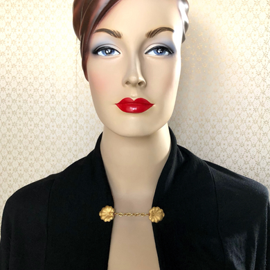 mannequin wearing a black jacket held together with a golden lily pad sweater clip