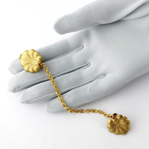 a golden lily pad sweater clip displayed on a grey gloved hand