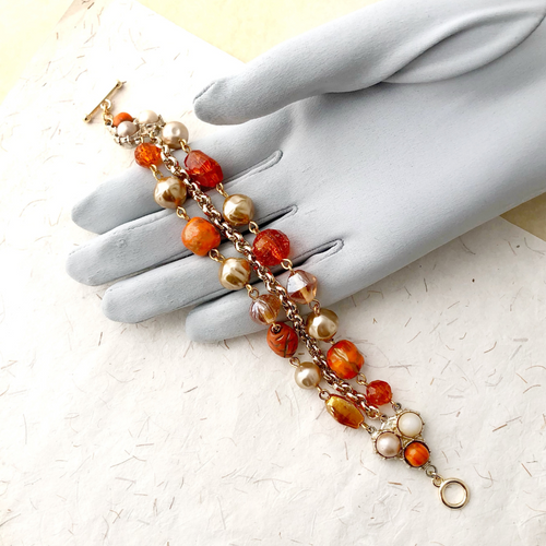 Bracelet with orange and gold beads on a gloved hand against a light background